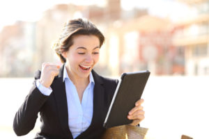 euphoric successful executive watching a tablet sitting in a bench in a park