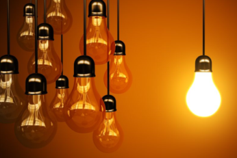 single light bulb glowing among other light bulbs with an orange background