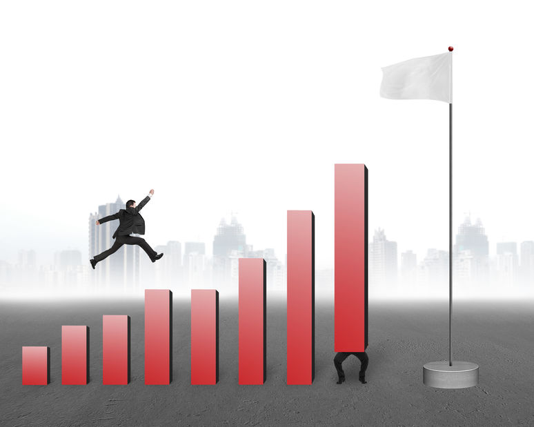 Businessman jumping over bar charts to blank flag with gray cityscape background signifying gamification